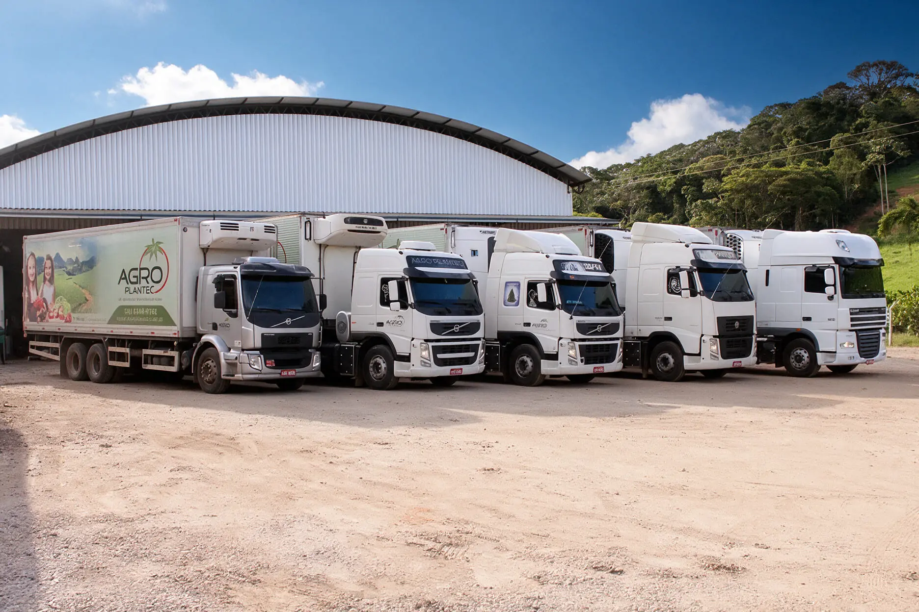 Caminhões refrigerados da frota Agroplantec estacionados em frente ao galpão